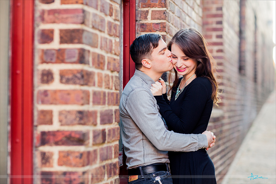 In the ally the couple shares a kiss during their engagement portrait session in downtown Raleigh, North Carolina
